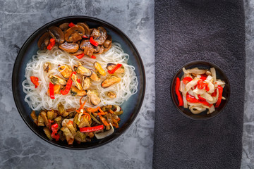 Traditional Asian food - rice noodles with seafood, salad, red pepper and fried mushrooms are on the side table. Top view