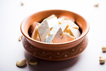 Fototapeta na wymiar Kaju Katli is a Diamond shape Indian sweet made using cashew sugar and mava, served in a plate or bowl over moody background. selective focus