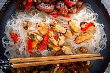 Rice noodles with seafood, salad, red pepper and fried mushrooms in a porcelain plate. Close-up. Top view