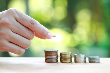 woman hand saving money on stacking coins with nature background