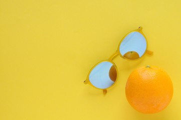 Orange fruit and yellow sunglasses isolated on yellow background for summer time with space for text.