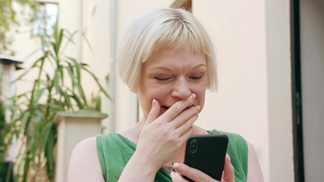 A pretty young blonde woman wearing a green dress sitting outside and using a phone. Close-up shot