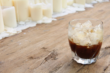 A glass of Shaken Espresso on wooden table decorated with candles that mixing ice cube with coffee for cold drink to enjoy hot weather of the summer. This photo has space for text and background.
