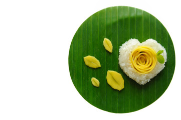 Mango sticky rice & coconut milk decorate as love shape & rose put on banana leaf. It's the famous dessert in summer of Thailand which is mango season isolated on white background with space for text.