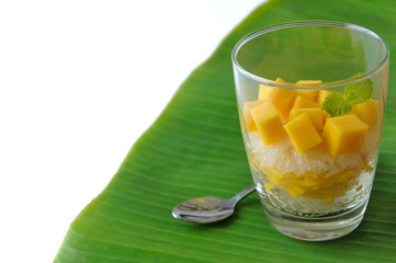 Mango sticky rice and coconut milk decorate in the glass put on banana leaf. It's the famous dessert in summer of Thailand which is mango season isolated on white background with space for text.