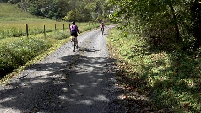 Camera pans with a woman on a mountain bike as she passes the camera and reveals her son riding with her on a rural, country road.