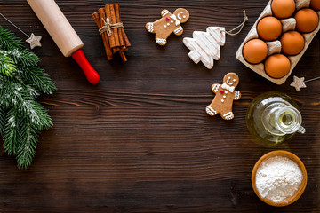 Obraz na płótnie Canvas Cook homemade gingerbread cookies for New Year party. Rolling pin, eggs, flour, cinnamon near gingerbread man and spruce branch on dark wooden background top view copy space