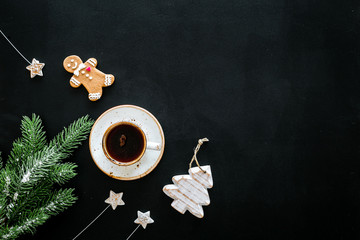 New Year gingerbread cookies. Gingerbread man near coffee, spruce branch, festive decoration on black background top view space for text