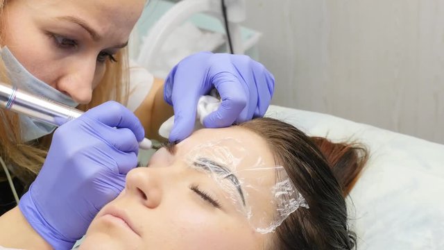 cosmetologist doing brows tattoo to female client. professional eyebrow permanent makeup. 4K