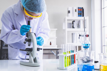 Young Asian woman research scientist preparing and analyzing microscope slides or looking through a microscope in research lab. Health care researchers working in life science laboratory concept