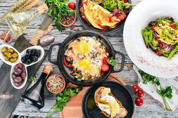 A set of food. Shakshuka, omelette, avocado salad, sandwich with poached egg. On a wooden background. Free space for text. Top view.