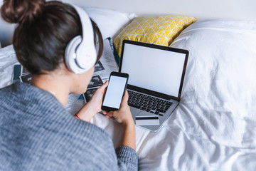woman using phone in bed laptop on background. white empty screens