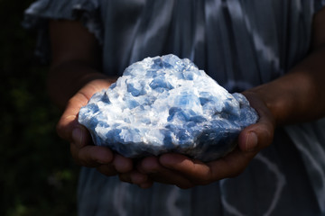 Close up of a woman holding a powerful healing blue calcite crystal in her hands in dark, moody...