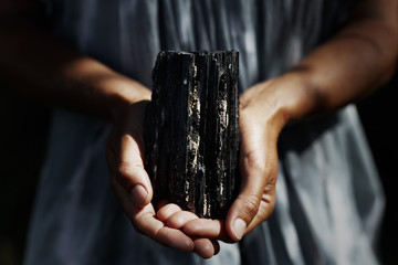 Woman's hands holding dark, powerful black tourmaline crystal in healing concept - obrazy, fototapety, plakaty