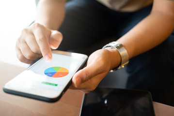 Asian woman looking at some charts on her mobile phone while sitting at coffee shop