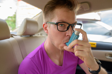 Face of man using asthma inhaler in back seat of car