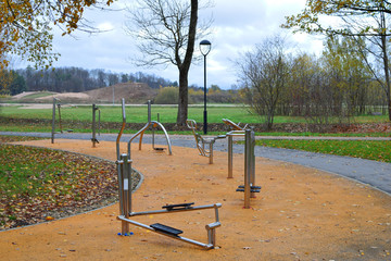 Different metal outdoor gym training machines for street workout standing outside in park in cold autumn morning.