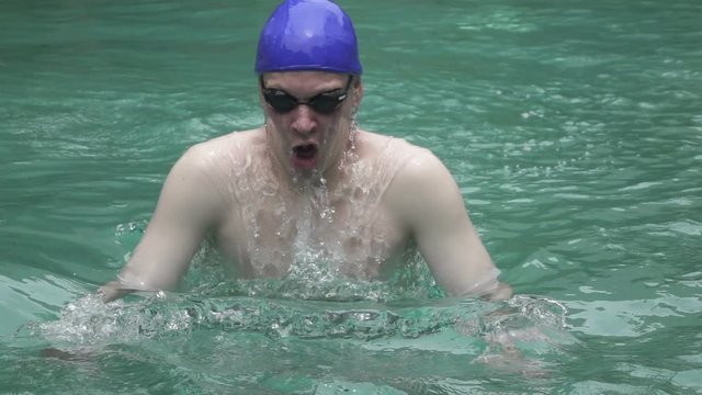 The young sports man floats in the pool a breast stroke on the camera,.slow motion