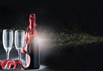 Wine bottle and glasses with red ribbon and golden glitters over black background © Leo Lintang