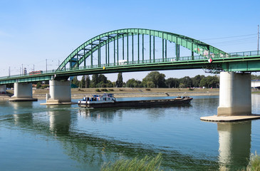 Cargo ship passing under the old railway bridge on Sava river