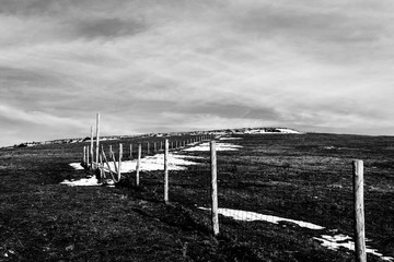 Wooden fence posts and barbed wire marking the property line of a prairie with dried grass and patches of snow under moody sky