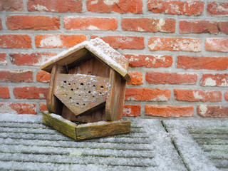 Small fallen wooden birdhouse against the side of a red brick house and covered in snow
