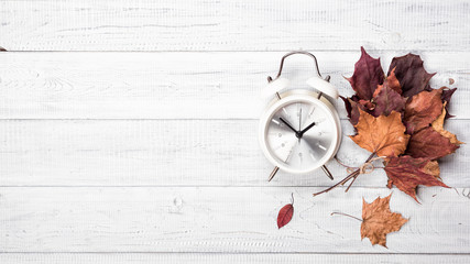 The vintage alarm clock and autumn fallen maple leaves on the white wooden table background, flat Lay, top view. Copy space for your text