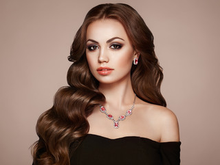 Brunette Girl with Long Healthy and Shiny Curly Hair. Care and Beauty. Beautiful Model Woman with Wavy Hairstyle. Make-Up and Black Dress
