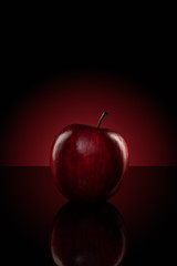 An apple isolated on reflective black board with red glowing light background