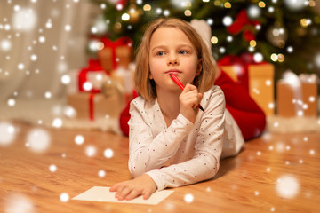 christmas, holidays and childhood concept - girl writing wish list or letter to santa at home