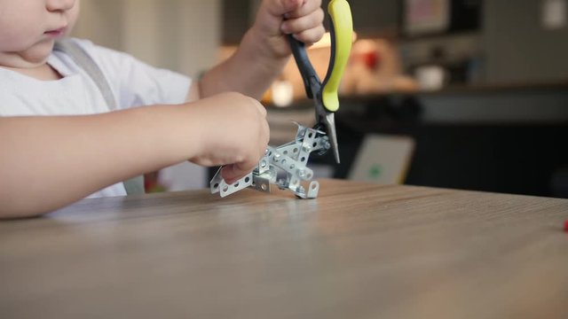 Serious little baby boy repairs meccano construction with needle-nose pliers