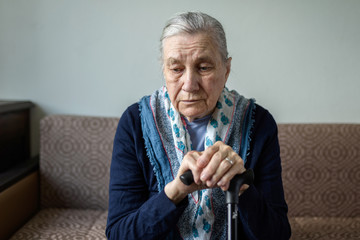 Sad old woman with a cane sitting on the couch