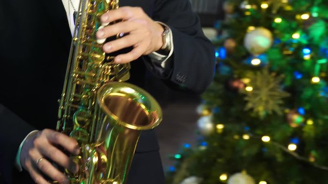 Man playing saxophone at new year party on background Christmas tree