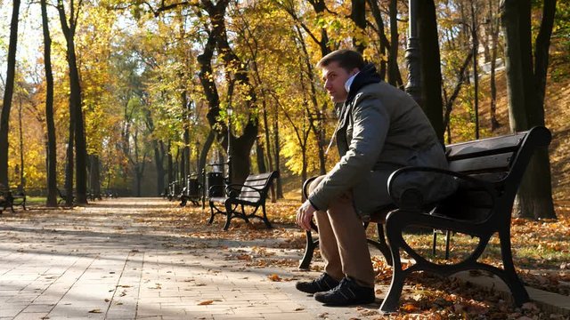 Young man with backpack sits on a bench in the autumn park.