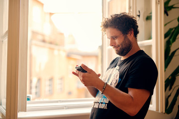 Cheerful young man texting and browsing the internet on his smart phone