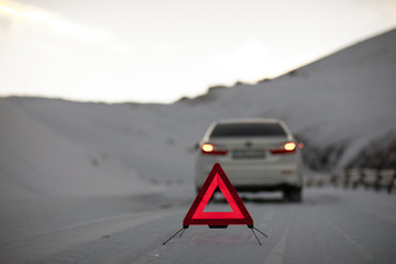broken car and an emergency sign on a snowy road