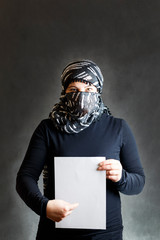 Naklejka premium Beautiful, girl in a black veil with a closed face on a gray tree. In the hands of a sheet of paper. Copy space.