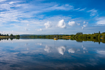 Obraz na płótnie Canvas Scenic landscape reflection with yellow boat and white clouds in blue water. Arrow Lake, Sligo, Ireland