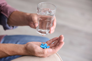 Man holding pills and glass of water, closeup