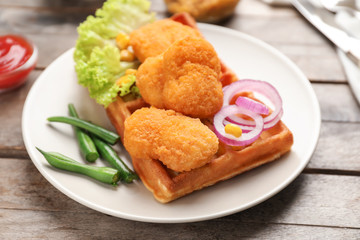 Plate with delicious waffle and chicken nuggets on wooden table