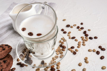 Glass cup of tasty milk with coffee beans on white table