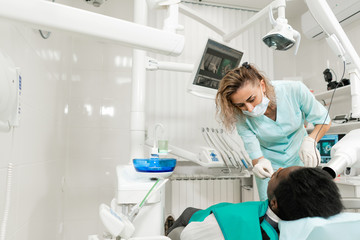 Obraz premium Woman dentist using x ray machine, patient lying on chair in dentistry. Young African American male with bad teeth. Medicine, health, stomatology concept.