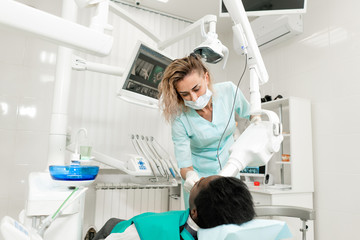Woman dentist using x ray machine, patient lying on chair in dentistry. Young African American male with bad teeth. Medicine, health, stomatology concept.