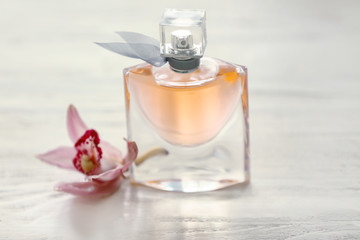 Bottle of perfume with tropical flower on white wooden table