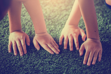 Children's hands on green artificial turf.