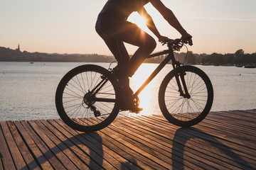 Fototapeta na wymiar man riding bicycle at sunset, cycling in summer, silhouette of cyclist near the lake