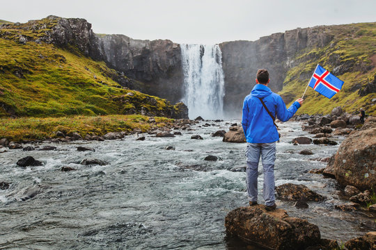 travel to Iceland, tourist holding icelandic flag near scenic waterfall