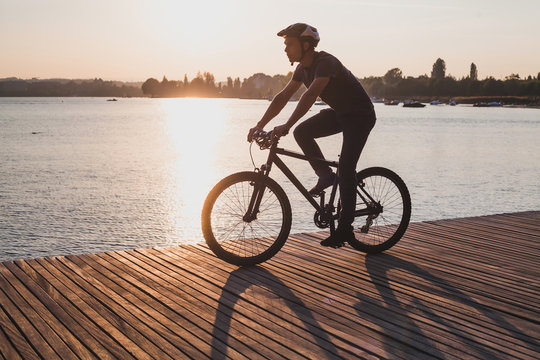 silhouette of man on bicycle in sunset city near lake, sport cycling active leisure