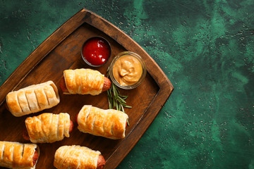 Wooden board with delicious sausage rolls on table