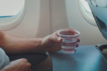 Naklejka premium Passenger drinking water in airplane during flight. Close up of hand holding glass in plane.